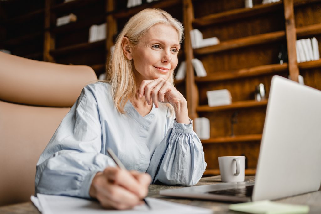 Smart caucasian mature middle-aged businesswoman CEO boss leader teacher writing, taking notes on laptop, e-learning , working remotely online in home office